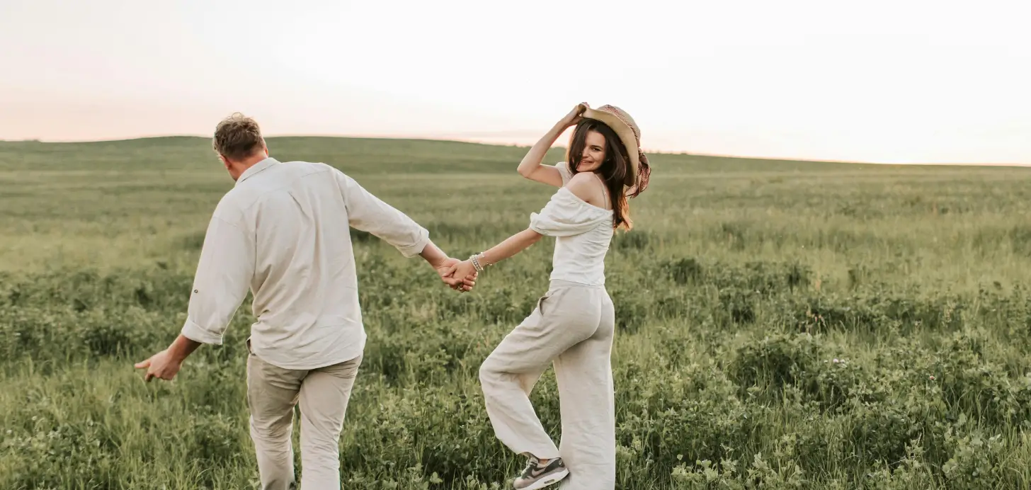 Ein Paar läuft Hand in Hand über eine grüne Wiese, wobei die Frau lachend zurückblickt und die lebendige Energie zwischen Introvertierten und Extrovertierten symbolisiert.
